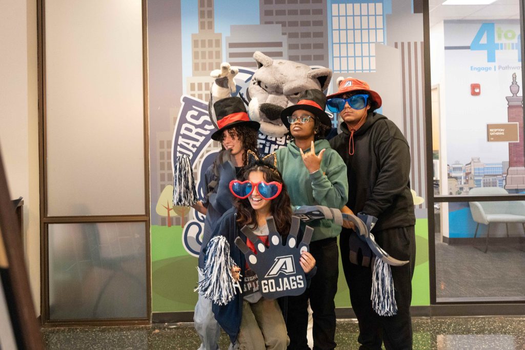 A group of men and women pose for a picture wearing props like bug sunglasses, hats and a pom pom. 