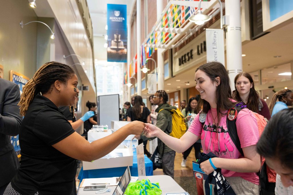 Two women stand talking at a tabling event.