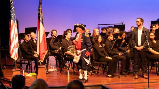 A man stands on stage next to several flags.