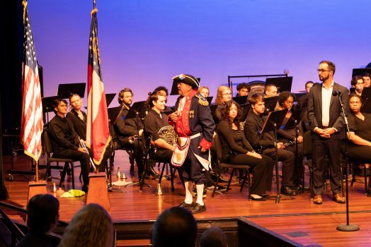 A man stands on stage next to several flags.