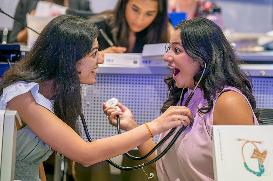 Two female medical students celebrate receiving their stethoscopes by testing them out on each other.