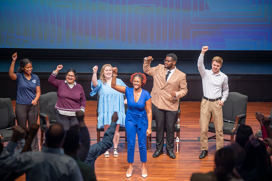 Six college students stand on a stage and cheer.