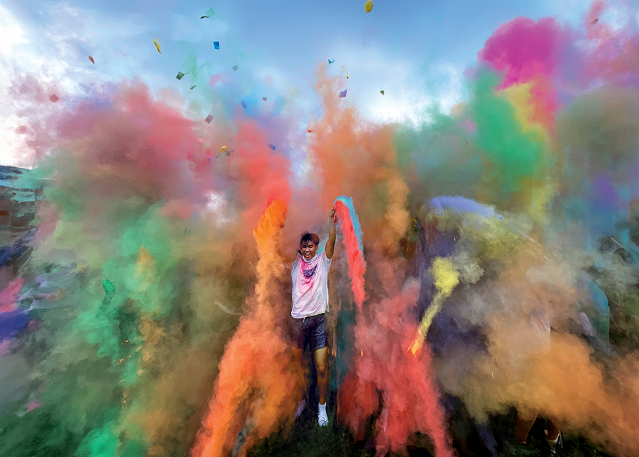 A college student flings colored powders into the air during a color run.