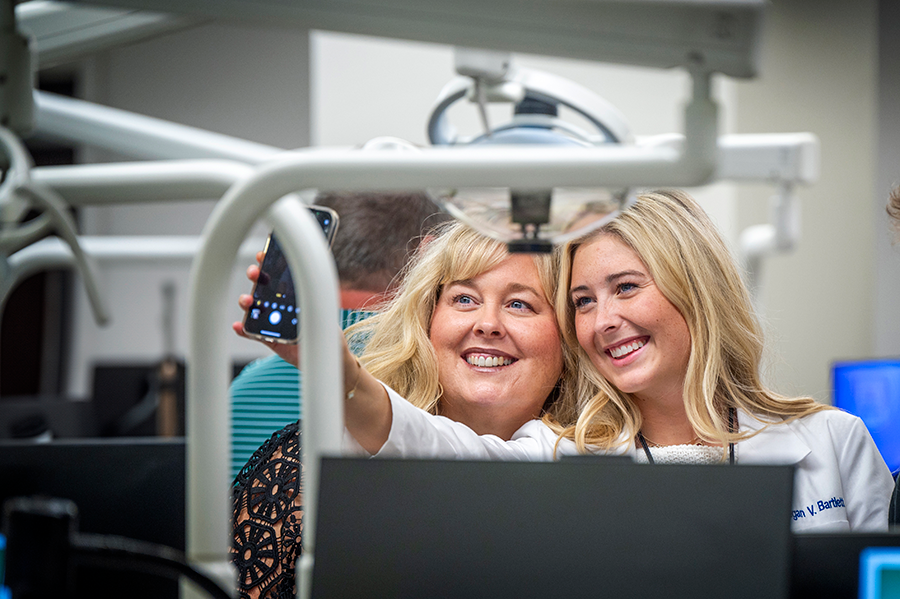 Two women huddle close together. One woman has her arm outstretched and is holding her phone to take a selfie.