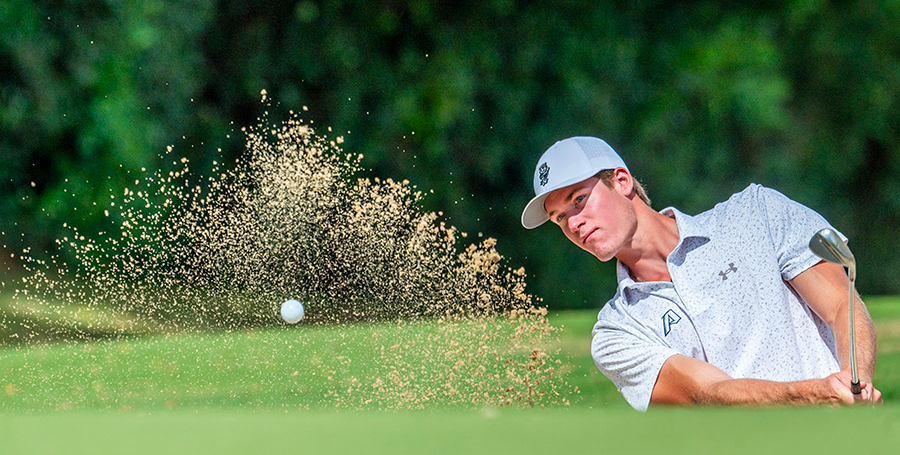 A male golfer hits a shot out of a sandtrap.