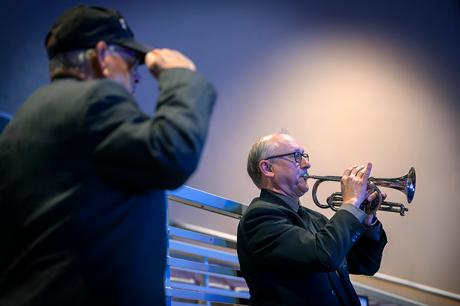 A man performs Taps on a trumpet while a veteran salutes.