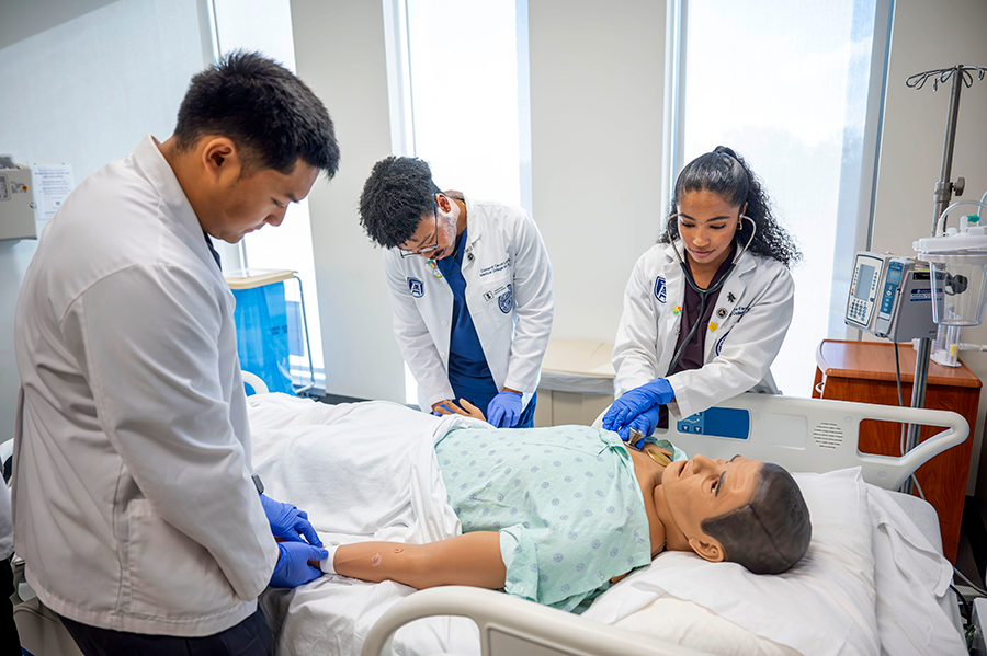 Three medical students practice life-saving techniques on a mannequin.