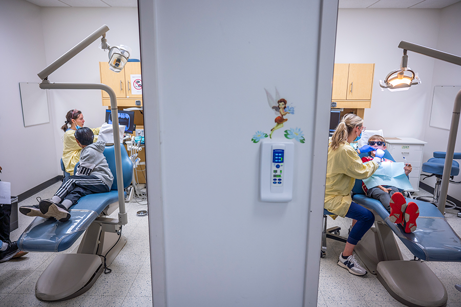 Two dentists in two adjoining rooms work on cleaning the teeth of children.