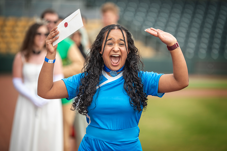 A female college student in a costume cheers and smiles as she holds an envelope.