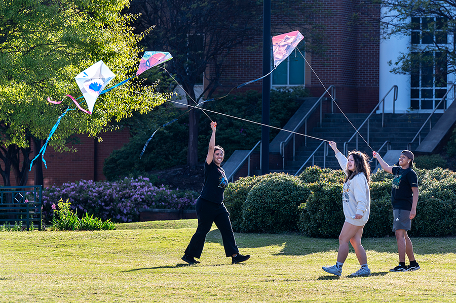 Three college students fly kites outside.