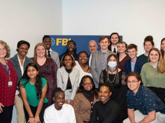 A group of college men and women huddle around a banner for the Federal Bureau of Investigation.