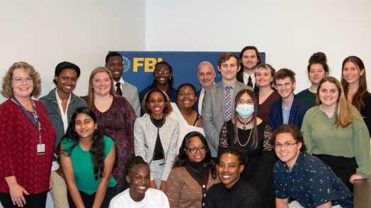 A group of college men and women huddle around a banner for the Federal Bureau of Investigation.