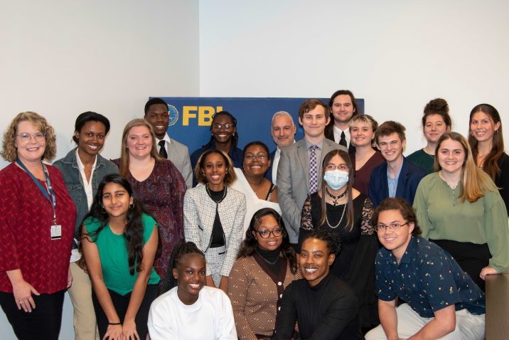 A group of college men and women huddle around a banner for the Federal Bureau of Investigation.