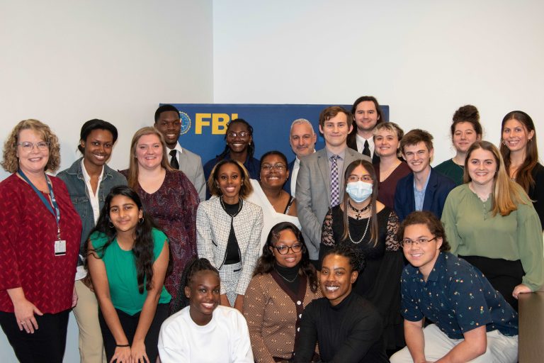 A group of college men and women huddle around a banner for the Federal Bureau of Investigation.