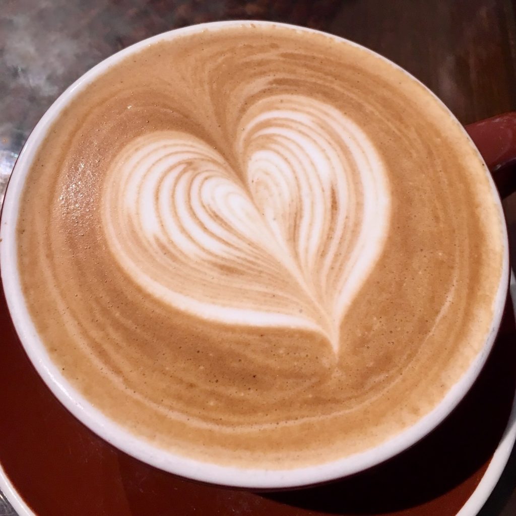 A latte in a mug. There is a heart design made out of the liquid.