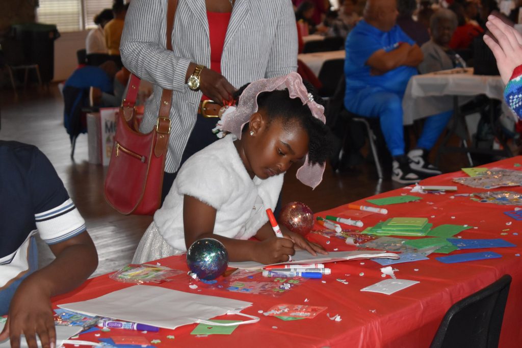 A young child uses a marker to decorate her holiday bag.