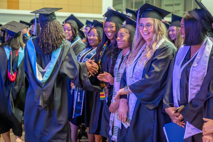 Various students in graduation robes are smiling.