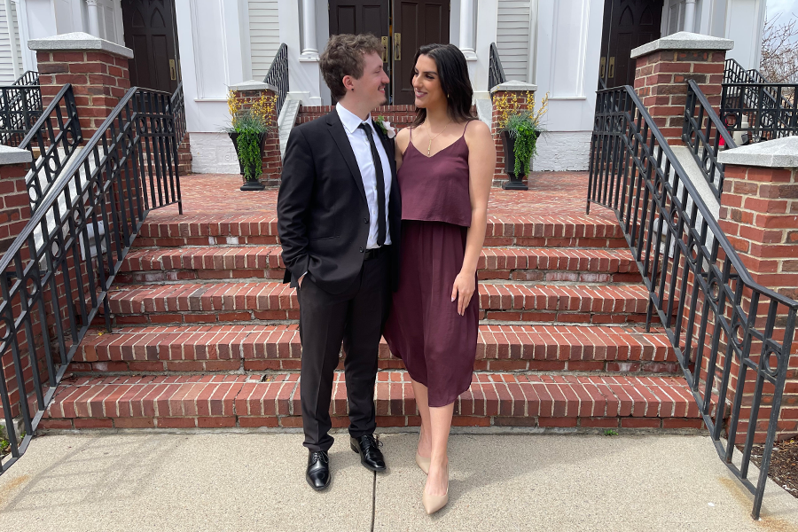 A man and a woman stand outside in front of a brick staircase. The man is wearing a tuxedo and the woman is wearing a nice dress.