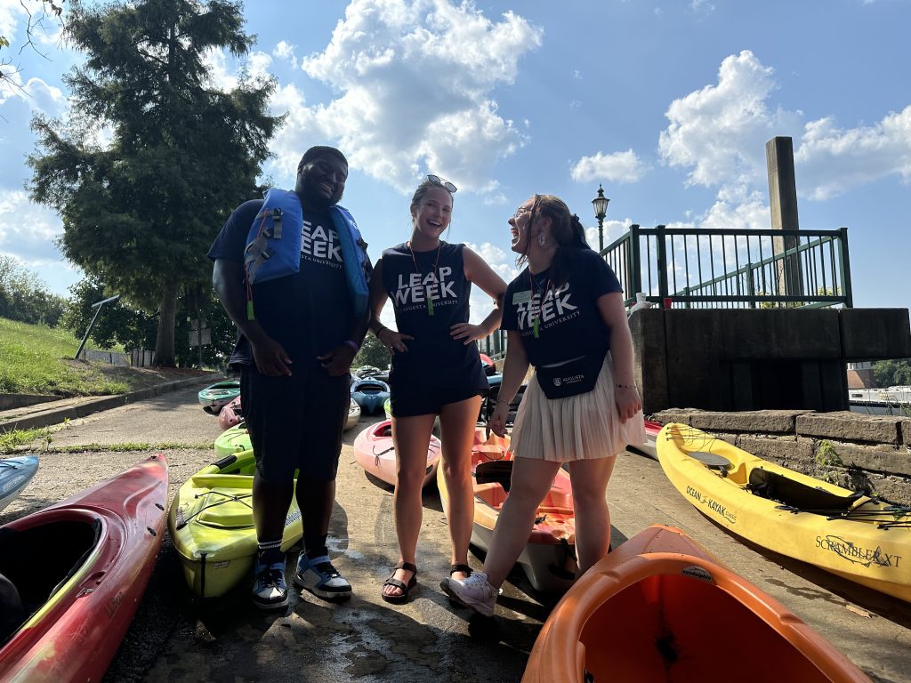 Two girls and a boy stand outside near kayaks.