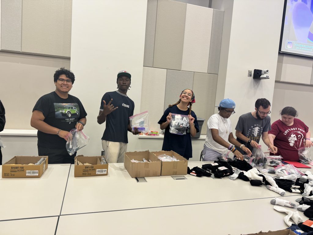 Several students smile for a picture while in line behind cardboard boxes.