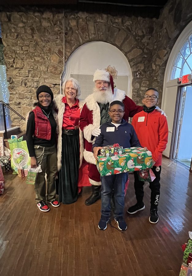 Kids standing with presents with two women and Santa Claus