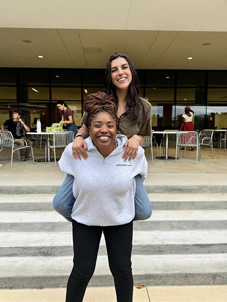 Two women, one is giving the other a piggy back ride.