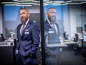 A man in a suit stands in the entryway to a large room filled with computer workstations.