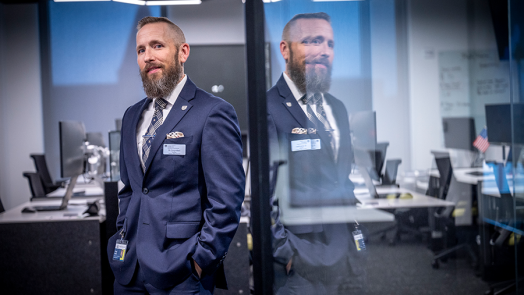 A man in a suit stands in the entryway to a large room filled with computer workstations.