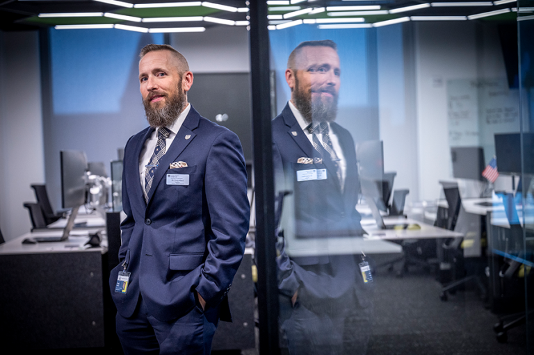 A man in a suit stands in the entryway to a large room filled with computer workstations.