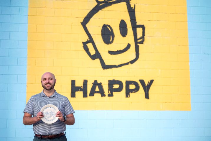 A man holds a painted plate in front of a mural.