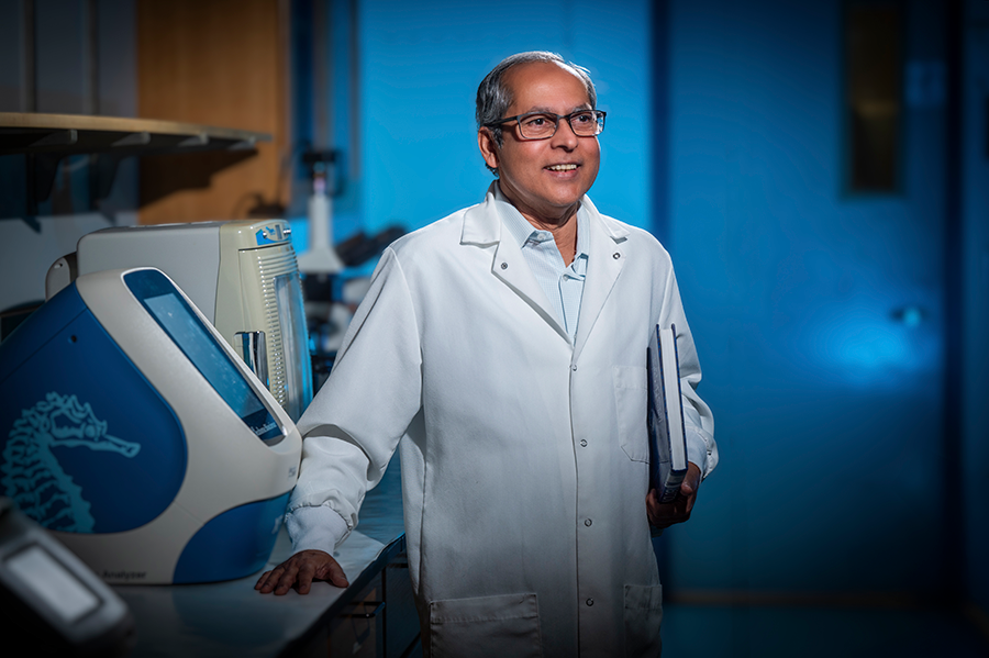 A man wearing a scientific lab coat holds a book while standing in a large laboratory.