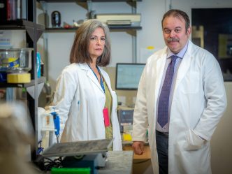 A man and woman in lab coats stand together in a scientific lab.