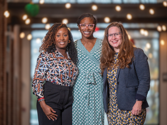 Three women stand in a long hallway.