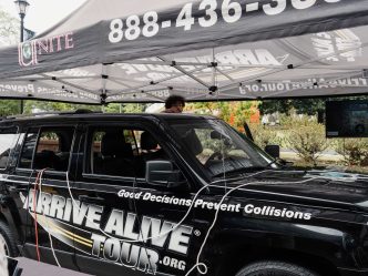 A black vehicle which has a sticker that reads "Arrive Alive Tour" is parked under a tent.