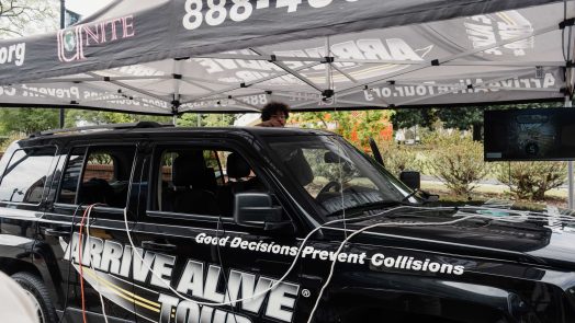 A black vehicle which has a sticker that reads "Arrive Alive Tour" is parked under a tent.