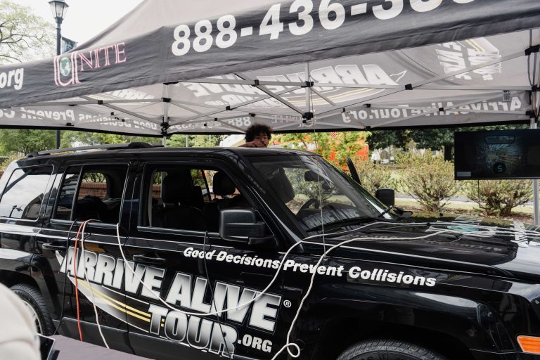 A black vehicle which has a sticker that reads "Arrive Alive Tour" is parked under a tent.