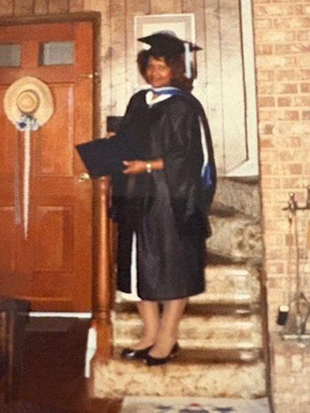 A woman wearing college graduation regalia standing on stairs.