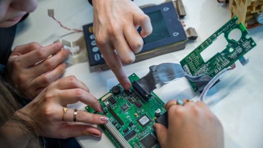 Close-up of students' hands working on assembling or repairing a circuit board.