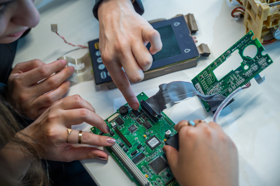 Close-up of students' hands working on assembling or repairing a circuit board.