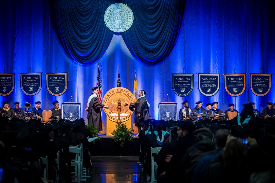 Student crosses the stage to shake the president's hand. 