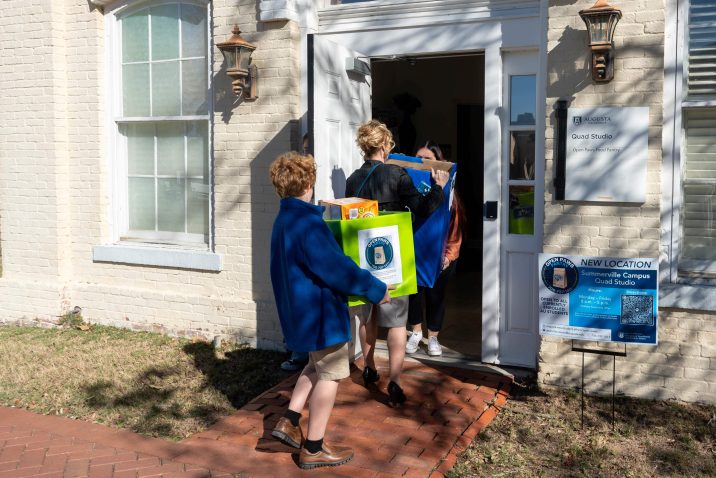 A woman and young boy walk into a building holding boxes.