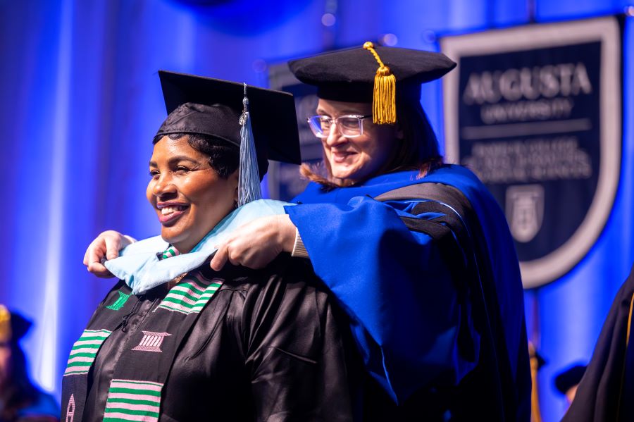 Female student receives a hood from her mentor. 