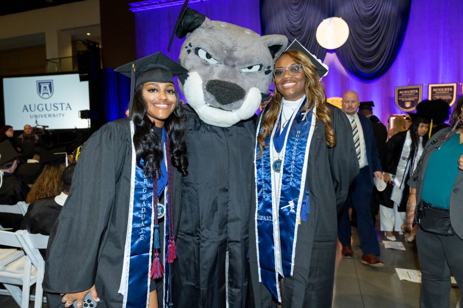 Two female students stand next to a cat mascot.