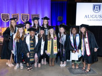 A large group of female college graduates, all wearing graduation caps and gowns, pose for a photo during a big ceremony.