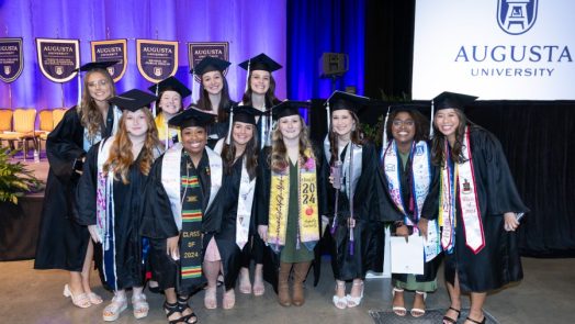 A large group of female college graduates, all wearing graduation caps and gowns, pose for a photo during a big ceremony.