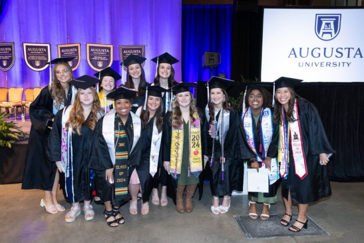 A large group of female college graduates, all wearing graduation caps and gowns, pose for a photo during a big ceremony.