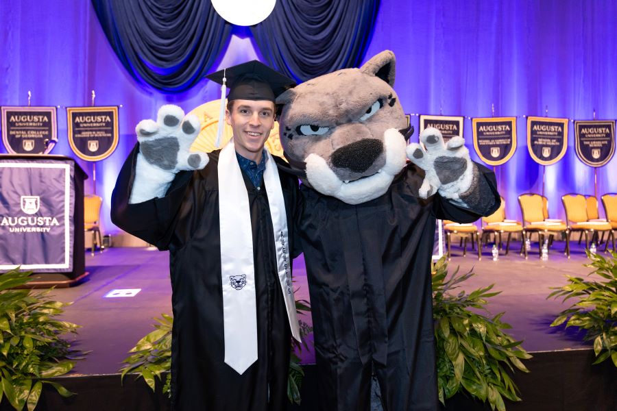 Male student holds up his hand with the cat mascot. 