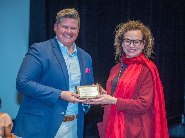 two women hold an award while smiling at the camera