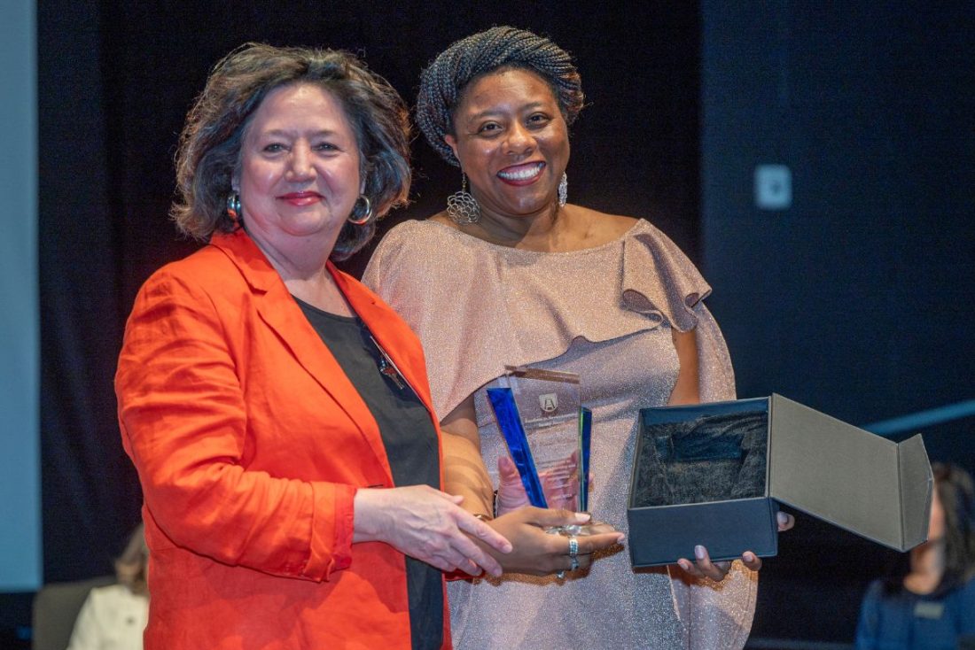 two women hold awards while smiling at the camera