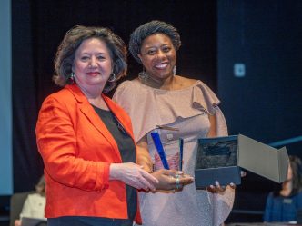 two women hold awards while smiling at the camera